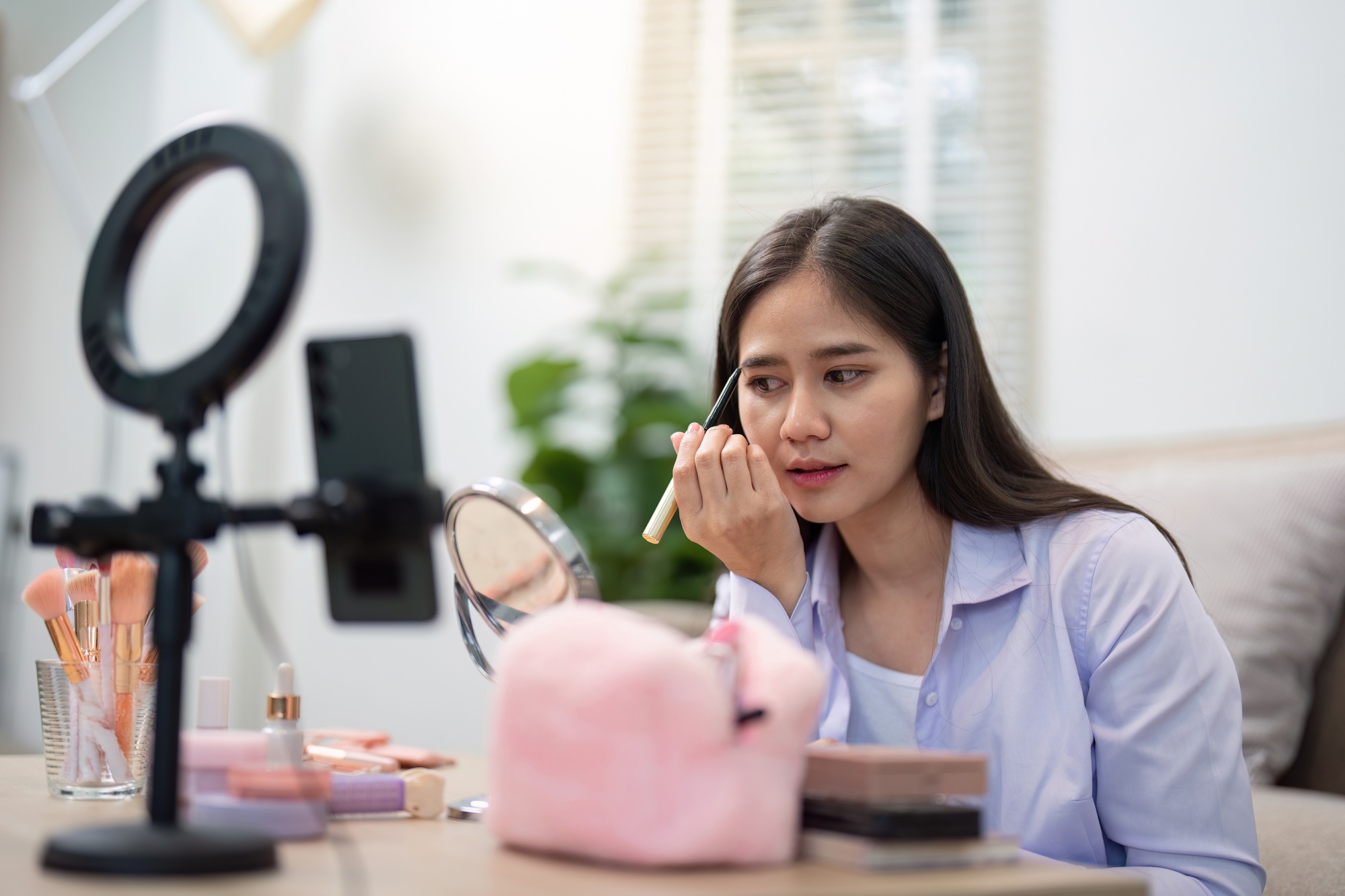 Asian woman refining eyebrow makeup with focused expression